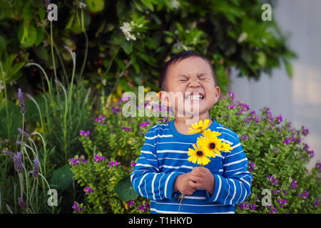 Eine fröhliche junge Holding ein paar handverlesene gelbe Blüten im Frühling, stand vor einer üppigen Garten. Stockfoto