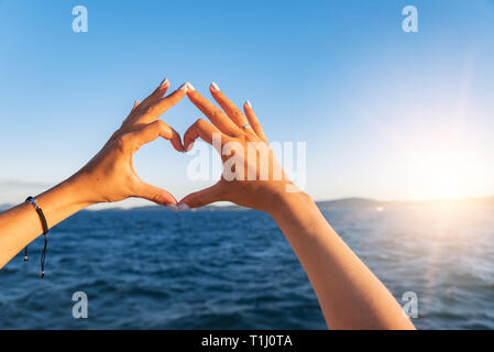 Junge weibliche schöne Hände auf dem Hintergrund des Meeres zeigen das Symbol des Herzens. Ferienhäuser - Konzept. Stockfoto