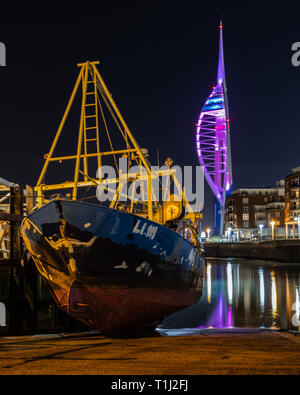 Spinnaker Tower leuchtet violett mit Fischerboot im Vordergrund ruht auf dem Kai Stockfoto