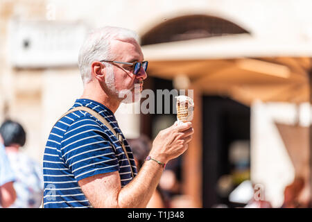 San Gimignano, Italien - 27. August 2018: Ein Mann essen Eis gelato Kegel Sorbet auf Quadrat in kleinen historischen mittelalterlichen Dorf in der Toskana während Summe Stockfoto
