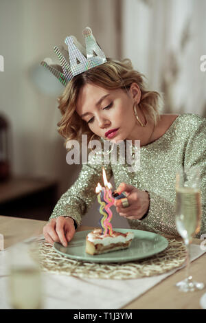 Frau in Gold Ring Ohrringe brennt die Kerze auf Kuchen Stockfoto