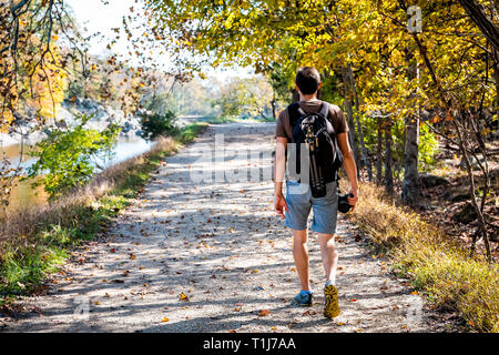 Junge Fotografen Mann zu Fuß zurück auf den Weg weg weg im Herbst Potomac River in den großen Fällen, Maryland mit buntes Laub und Rucksack Stativ Stockfoto