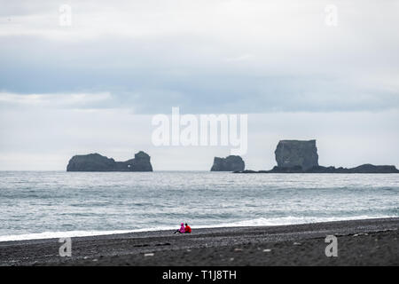 Vik, Island zwei Personen Paar auf schwarzem Sand Beach Ocean horizon Rock Formation Dyrholaey, Kirkjufjara an der Südküste Stockfoto