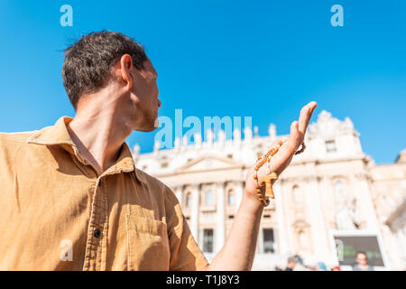 Junger Mann pilgrim Holding in den Händen Holz handgefertigten italienischen Kreuz katholische Rosenkranz mit bokeh Hintergrund der Vatikan Kirche St. Peter's Square Basilika du Stockfoto