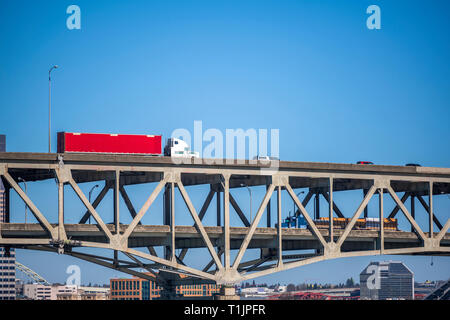 Big rigs Semi Trucks bewegen sich in entgegengesetzte Richtungen auf den verschiedenen Ebenen der zweistufige Überführung Brücke mit einem anderen Verkehr vor dem Hintergrund der hohen Stockfoto