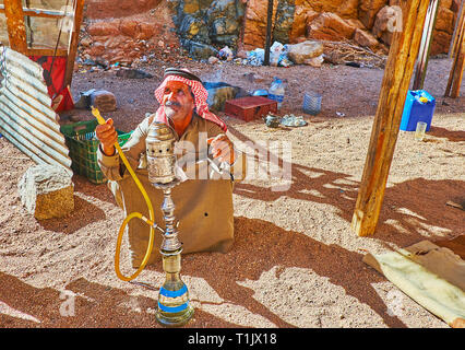 DAHAB, Ägypten - Dezember 16, 2017: Die traditionell gekleidete ältere Beduinen, auf dem Boden sitzend in der Wüste, behandelt die touristische schalten Shisha und Kaffee, o Stockfoto