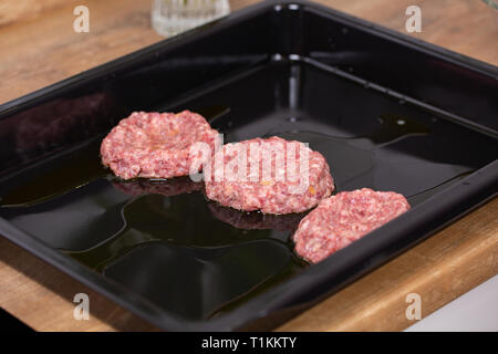 Backblech mit Raw burger Frikadellen oder Schnitzel oder Frikadelle, Nahaufnahme. Prozess des Kochens Stockfoto