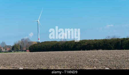 Windkraftanlage mit einem hellblauen Himmel als Hintergrund und eine karge Feld im Vordergrund. Stockfoto