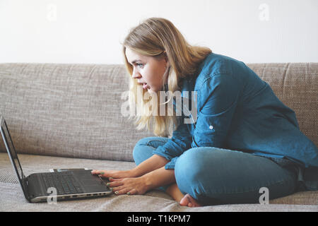 Junge Frau mit Laptop zu Hause sehen etwas Unglaubliches auf dem Computer geschockt. Schlechte Nachrichten Konzept, Kündigung und Kündigungsfrist von Boss Stockfoto