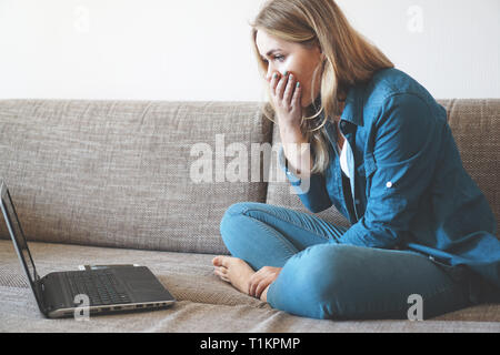 Junge Frau mit Laptop zu Hause sehen etwas Unglaubliches auf dem Computer geschockt. Schlechte Nachrichten Konzept, Kündigung und Kündigungsfrist von Boss Stockfoto