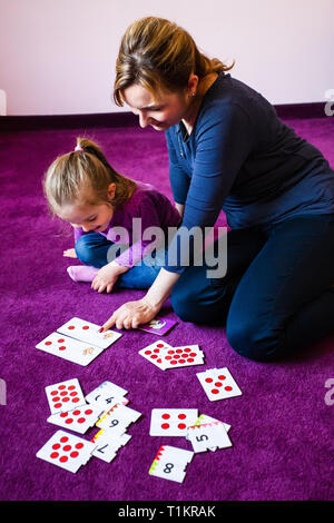 Mutter Lehre zählen ihre kleine Tochter mit Card Game, das auf einem Teppich zu Hause sitzen Stockfoto