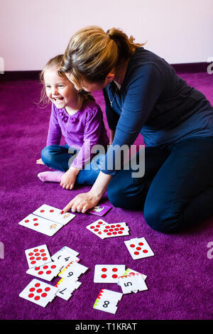 Mutter Lehre zählen ihre kleine Tochter mit Card Game, das auf einem Teppich zu Hause sitzen Stockfoto