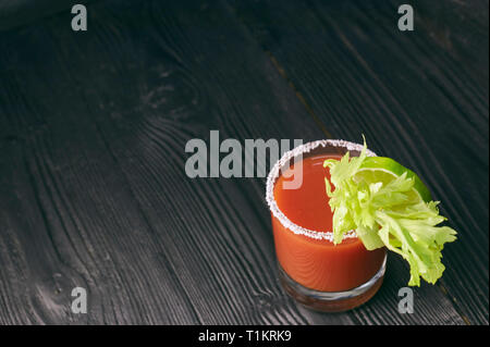 Cocktail Bloody Mary mit Kalk und Sellerie, Salz und Snacks in einem Glas auf einem schwarzen Holztisch. Stockfoto