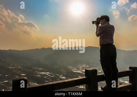 Yuanyang County, Yunnan, China - 2014: Touristische stehend auf einem oberen Zaun Geländer eine Fotografie der Reisterrassen bei Bada Yuanyang Stockfoto