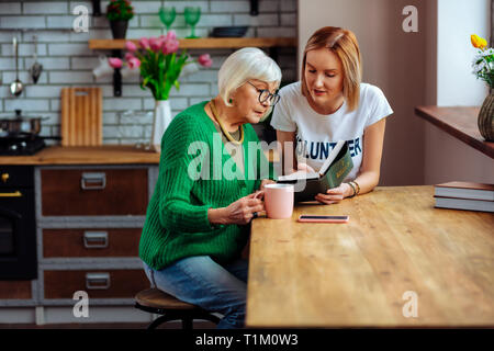 Rentner hören junge Dame Lesen der Bibel sitzen am Tisch Stockfoto