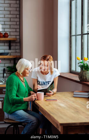 Lächelnde Dame lesen Holly Bibel während Rentner ihr zuhören Stockfoto