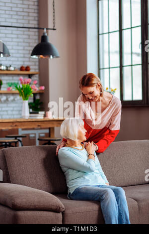 Reizende junge erwachsene Dame sanft die Hand auf die Schulter der Mutter Stockfoto