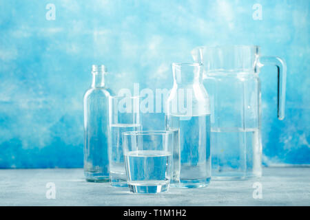 Gruppe von leeren Gläsern und Flaschen mit klarem Wasser auf blauem Hintergrund Stockfoto