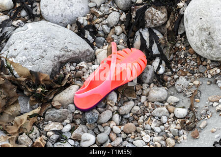 Ein helles Rosa Plastik jelly Schuh verlassen auf einem steinigen Strand verloren geht oder Stockfoto