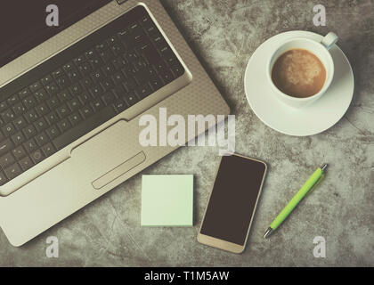 Laptop, Mobiltelefon und Kaffee Tasse auf Schreibtisch gegen Grunge Hintergrund Stockfoto