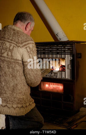 Mann Einspeisung in prasselnden Feuer im alten Stil Holzofen in einem Ferienhaus zala Ungarn anmelden Stockfoto