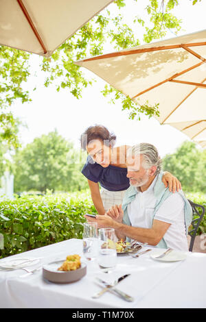 Älteres Ehepaar mit Smart Phone im Patio Restaurant Stockfoto