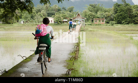 HPA EIN, MYANMAR - 13 Jun 2014: Kinder in Schuluniform fahren mit dem Fahrrad auf eine konkrete Brücke über die Reisfelder, um Hpa eine Stadt im südlichen Stockfoto