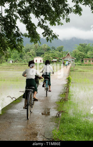 HPA EIN, MYANMAR - 13 Jun 2014: Kinder in Schuluniform fahren mit dem Fahrrad auf eine konkrete Brücke über die Reisfelder, um Hpa eine Stadt im südlichen Stockfoto