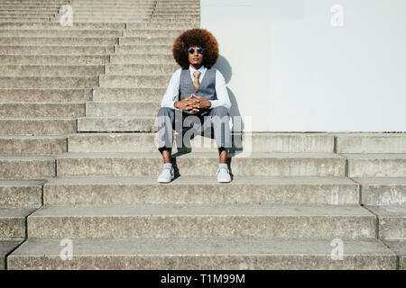 Portrait zuversichtlich, kühl, gut gekleideten jungen Mann mit Afro sitzen auf städtischen Schritte Stockfoto