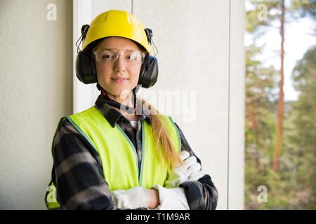 Porträt einer jungen weiblichen Bauarbeiter in harten Hut bohren Beton Wand mit einer Bohrmaschine und einem Lächeln in die Kamera. Bau und Renovierung. FEM Stockfoto