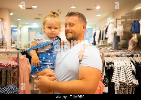 Vati mit Kind Mädchen wählt und kauft Kleidung im Store, Konzept der Vaterschaft. Stockfoto