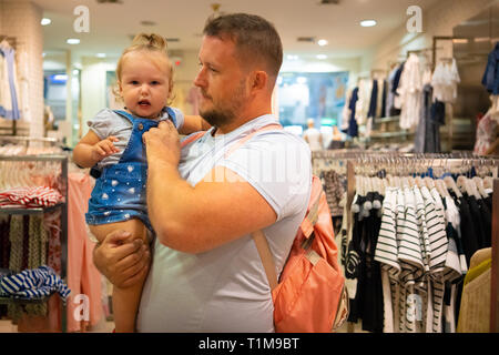 Vati mit Kind Mädchen wählt und kauft Kleidung im Store, Konzept der Vaterschaft. Stockfoto