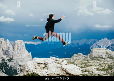 Unbeschwerter Junge, der auf dem Berg über Felsen springt, Naturpark drei Zinnen, Südtirol, Italien Stockfoto