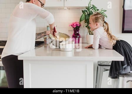 Neugierige Mädchen beobachten Mutter backen in der Küche Stockfoto
