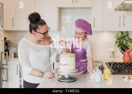 Mutter und Tochter dekorieren Kuchen in der Küche Stockfoto