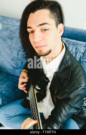 Junger Mann, der mit seiner E-Gitarre auf dem Sofa seines Hauses lernen. Stockfoto