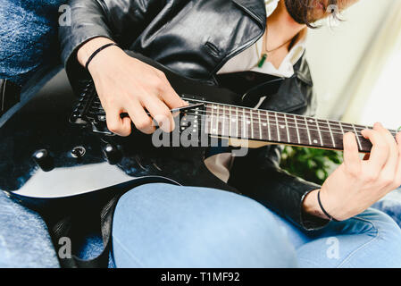 Junger Mann, der mit seiner E-Gitarre auf dem Sofa seines Hauses lernen. Stockfoto
