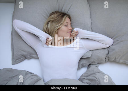 Hübsche blonde Frau erstreckt sich im Bett Stockfoto