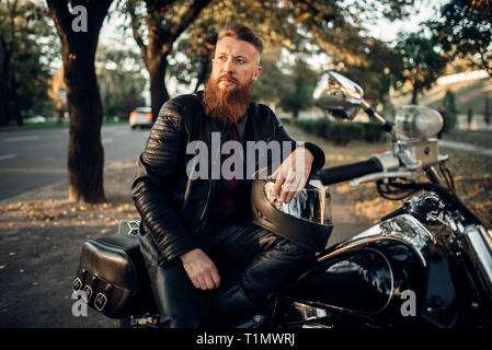 Biker auf dem Boden sitzend gegen seinen Chopper Stockfoto