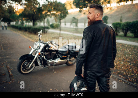 Bärtige Biker mit Helm geht zu seinem Häcksler Stockfoto