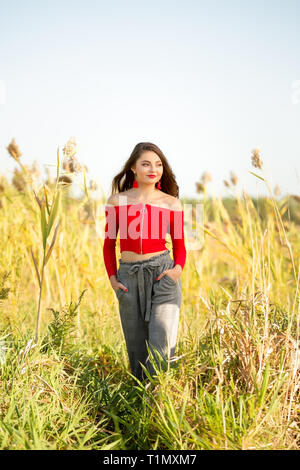 Eine schöne weibliche caucasain High School Girl in Red Top Pullover zu Fuß außerhalb in einem Bauernhof Feld Sommer. Stockfoto