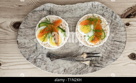 Zwei Reiskräcker mit Gurke, Ei, geräuchertem Lachs und Dill, zwei Vintage silber Gabel auf dem Schneidebrett Stockfoto