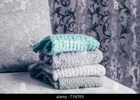 Stilvolle gestrickte Pullover in Pastelltönen auf Samtigen Stoff Sofa mit einem Vintage Vorhang Hintergrund stack gefaltet. Close Up, kopieren. Stockfoto