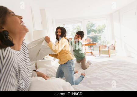 Verspielte Mutter und Kinder genießen Kissenschlacht auf dem Bett Stockfoto