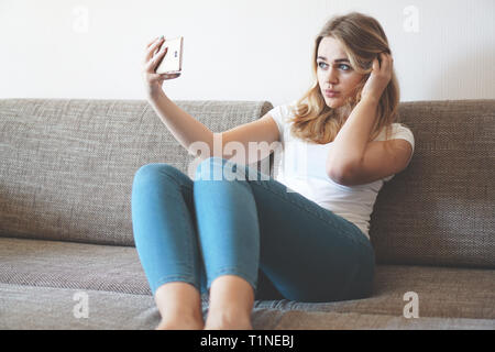 Schuss eine glückliche junge Frau, die mit ihrem Handy selfie beim Sitzen im Wohnzimmer Stockfoto