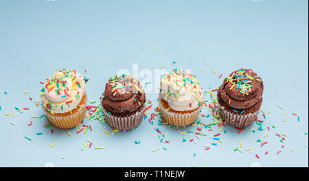 Cupcakes auf Blau pastell Hintergrund. Vier cupcakes Vanille und Schokolade mit bunten Streuseln, kopieren Raum Stockfoto