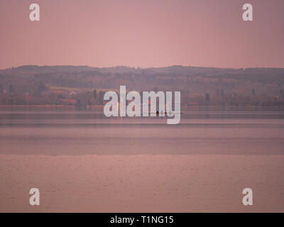 Bild der Ammersee mit Ruderboot und Dorf mit Kirche im Hintergrund, während Sie im Sonnenuntergang in Bayern Deutschland Stockfoto