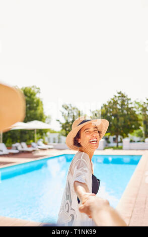 Glückliche Ehefrau führenden Mann an der Hand bei Sunny Resort Pool Stockfoto