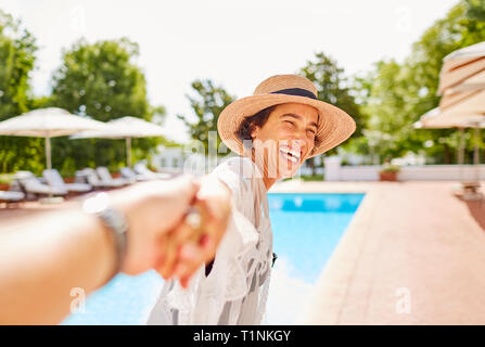 Glückliche Ehefrau führenden Mann an der Hand bei Sunny Resort Pool Stockfoto