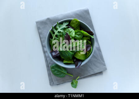 Schüssel mit Mix frische Blätter aus Rucola, Spinat und Rüben Blätter auf grau Holz- Hintergrund. Vegetarisches Essen Konzept. Selektive konzentrieren. Ansicht von oben Stockfoto